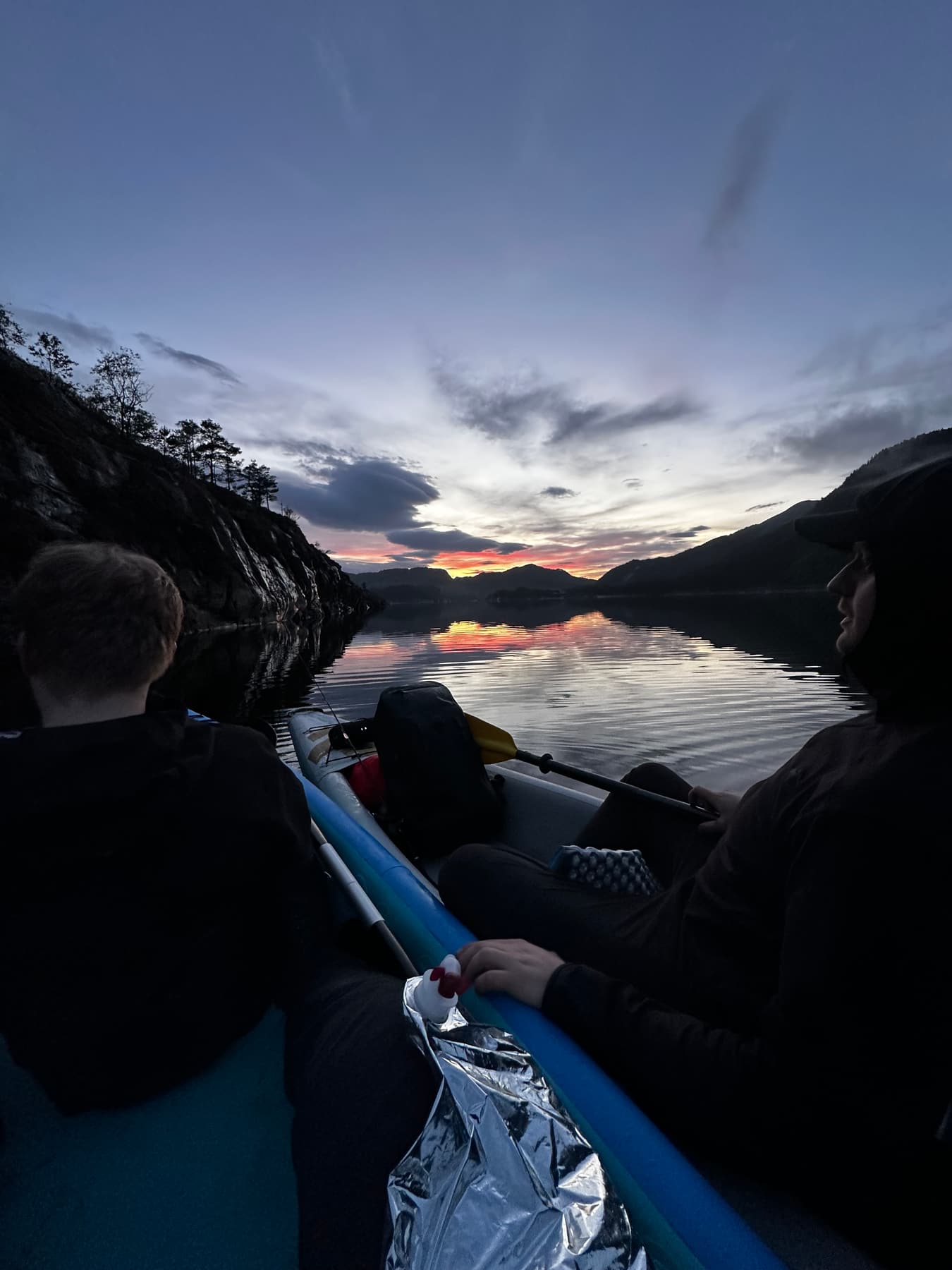 To personer i kajakk på en fjord i solnedgang